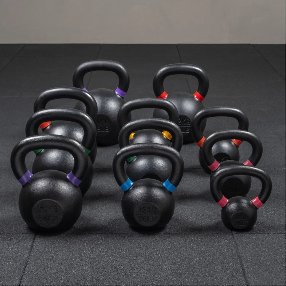 Set of black kettlebells with color-coded handles on a dark floor.