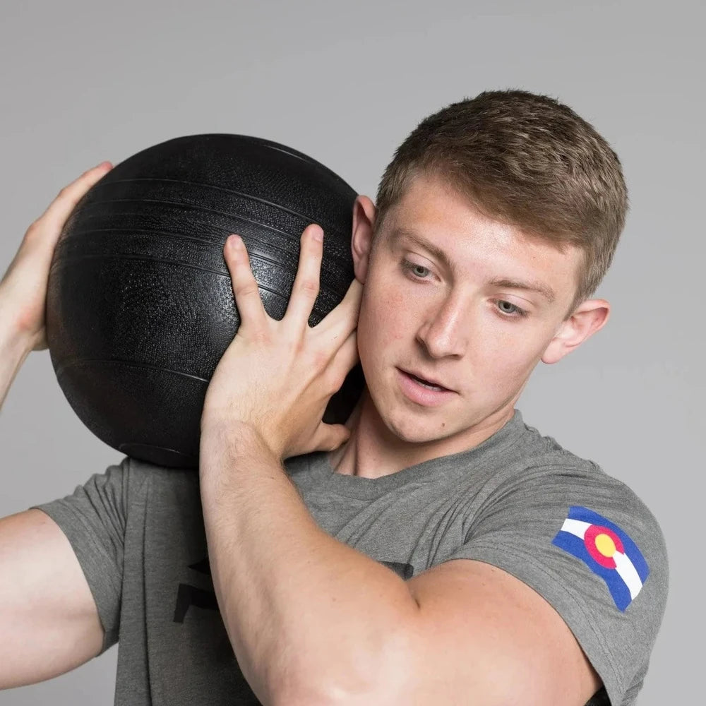 Person holding a black slam ball against a gray background