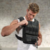 Man adjusting a black weighted vest against a brick wall.