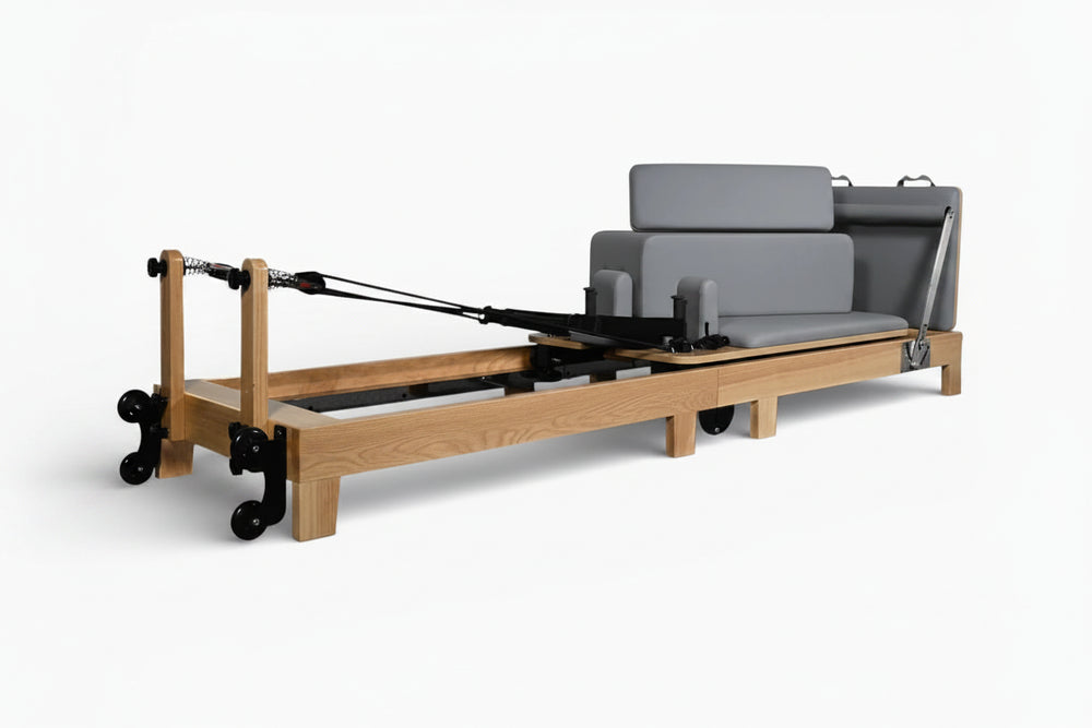 Pilates reformer with wooden frame and gray cushion on a white background