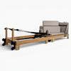 Wooden reformer exercise machine with cushioned seat on a white background
