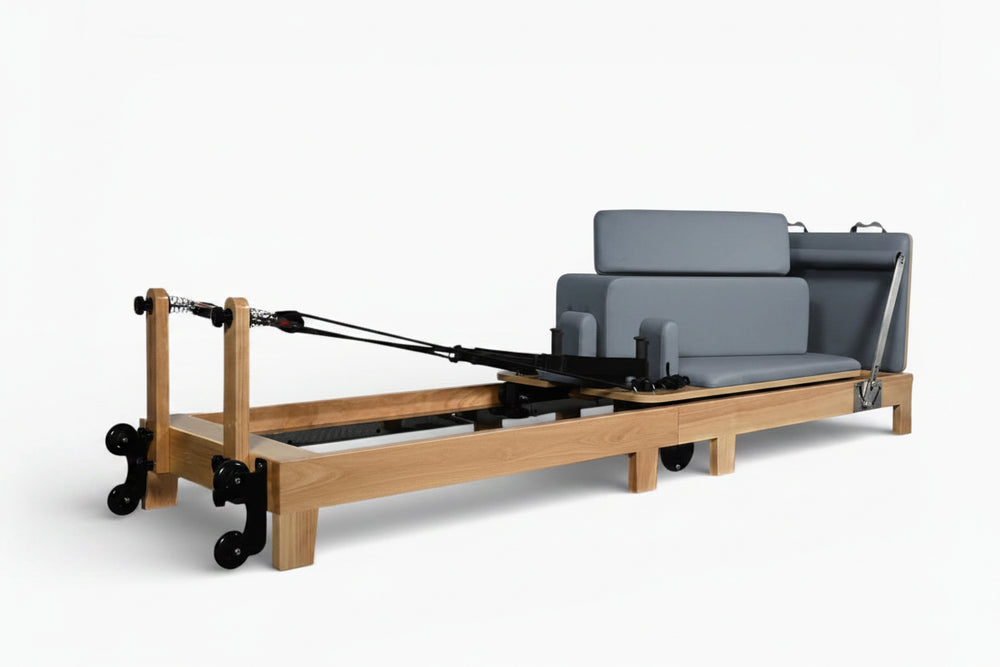 Pilates reformer with wooden frame and gray cushion on a white background