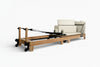 Pilates reformer with wooden frame and white cushioned seat on a white background