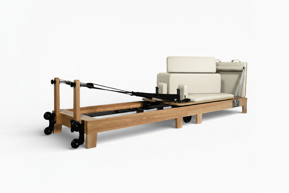 Pilates reformer with wooden frame and white cushioned seat on a white background