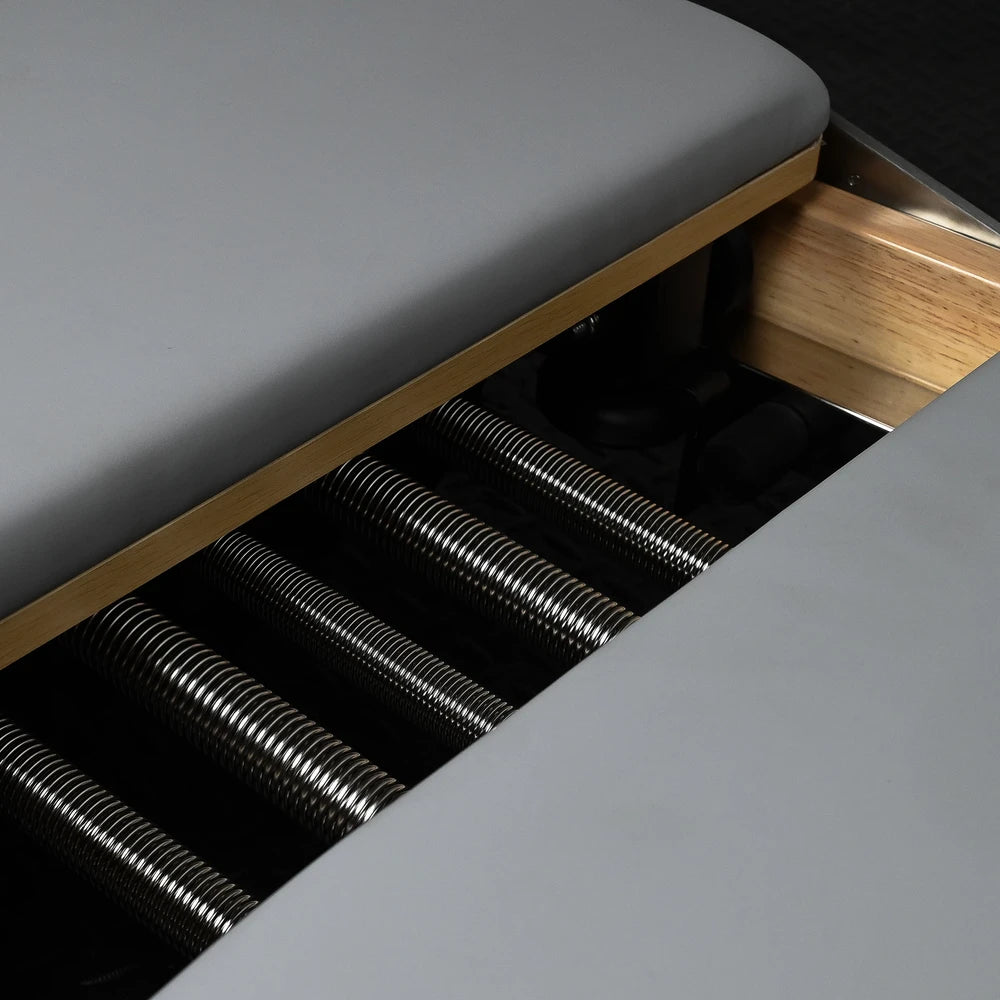 Gray cushioned pilates reformer with metal springs visible underneath.
