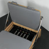 Gray cushioned pilates machine with a wooden base and spring mechanism on a black floor