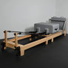 Pilates reformer with wooden frame and gray cushion on a dark floor.
