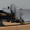Gray cushioned pilates machine with wooden base on a gray background