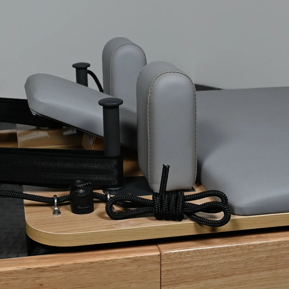 Gray cushioned pilates machine with wooden base on a gray background