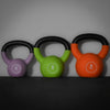 Three colorful kettlebells with weight labels on a dark surface and gray background