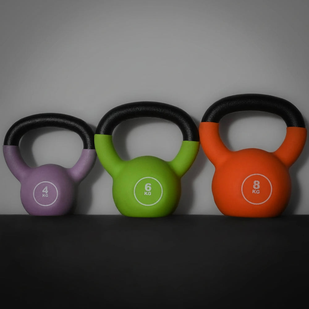 Three colorful kettlebells with weight labels on a dark surface and gray background