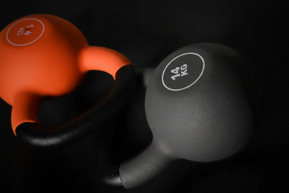 Two kettlebells, one orange and one black with '14 KG' label, on a dark background.