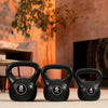 Three black kettlebells with weight markings on a wooden floor.