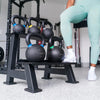 Person in light blue leggings and white sneakers standing next to a black kettlebell rack with kettlebells.