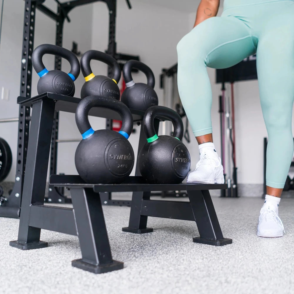 Person in light blue leggings and white sneakers standing next to a black kettlebell rack with kettlebells.