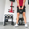 Person holding a kettlebell in a gym setting with various weights and exercise equipment.