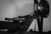 Close-up of a black rowing erg machine with footrest and pedals on a gray background