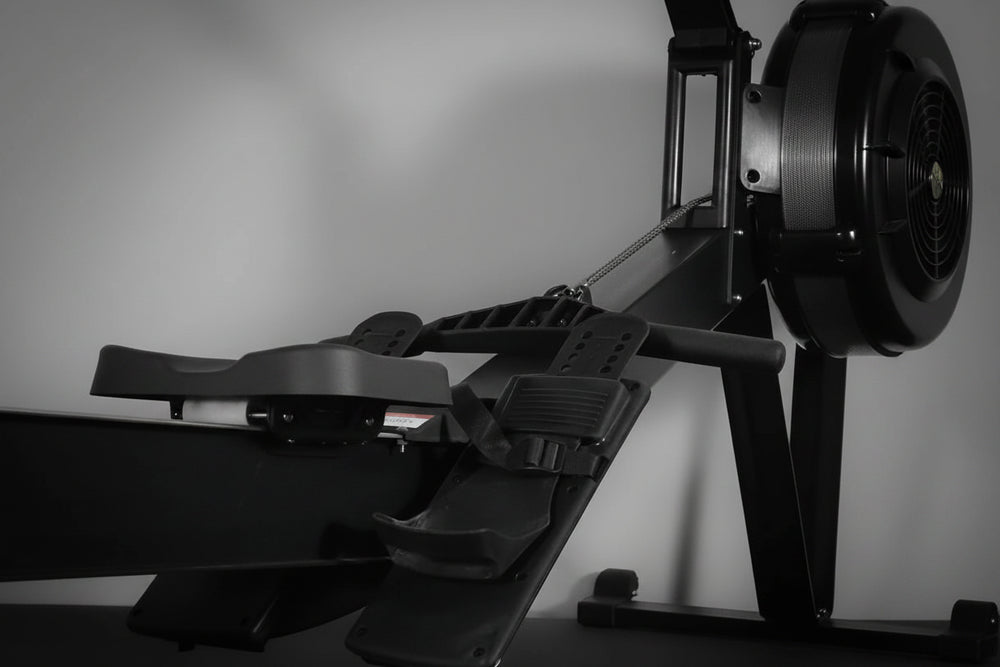 Close-up of a black rowing erg machine with footrest and pedals on a gray background