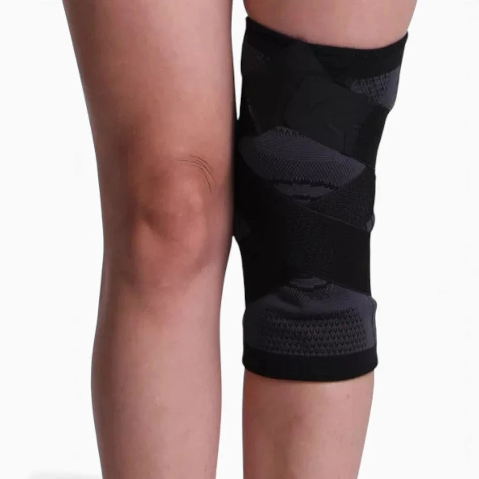 Black knee brace on a person's knee with a plain background