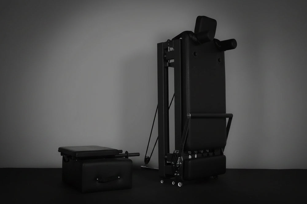 Black Pilates reformer and mat against a gray background