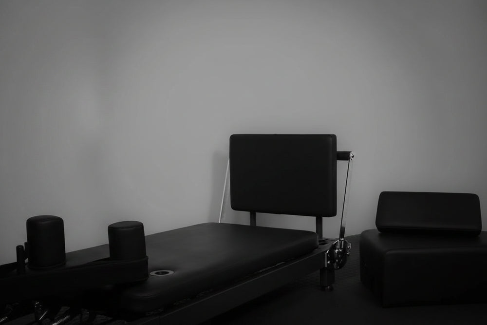 Black pilates reformer against a plain wall.