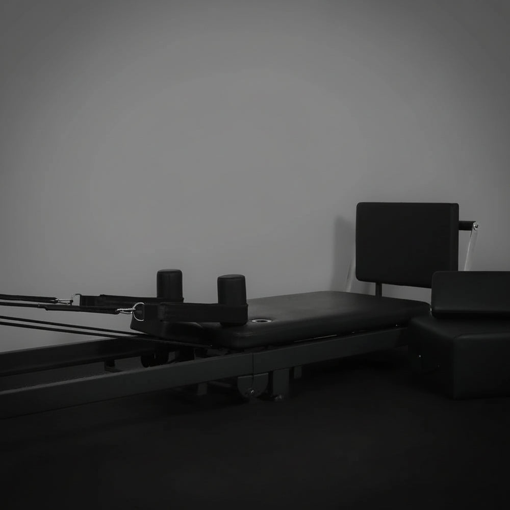 Black pilates exercise machine against a plain wall.