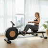 Woman exercising on a rowing machine in a bright room with large windows.