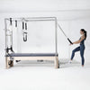 Woman exercising on a Pilates reformer machine in a white room