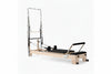 Pilates reformer tower in oak with black seats on a white background