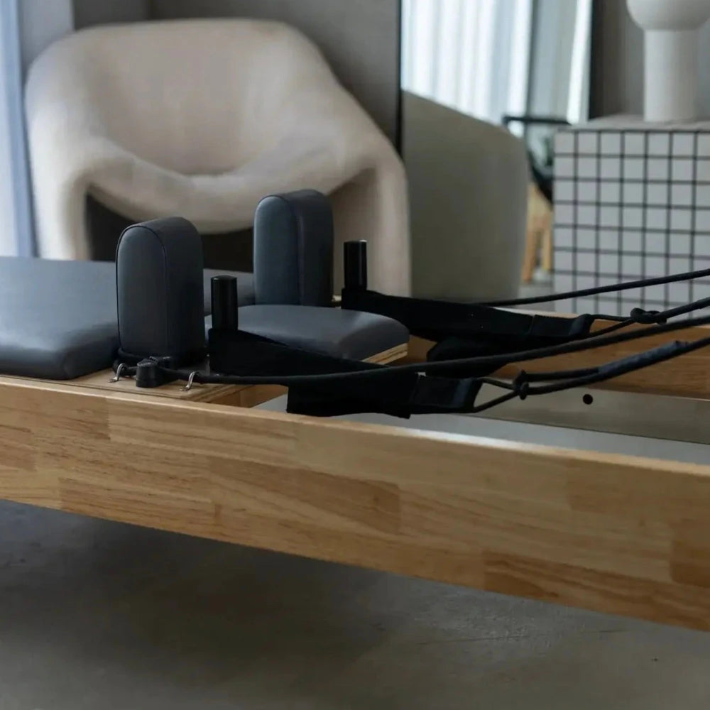 Oak Pilates reformer machine with dark padding in a home gym