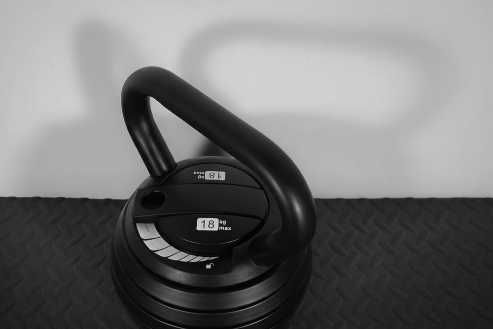 Black kettlebell with adjustable weights on a black textured floor