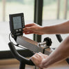 Person adjusting settings on a cycling machine with a digital display.
