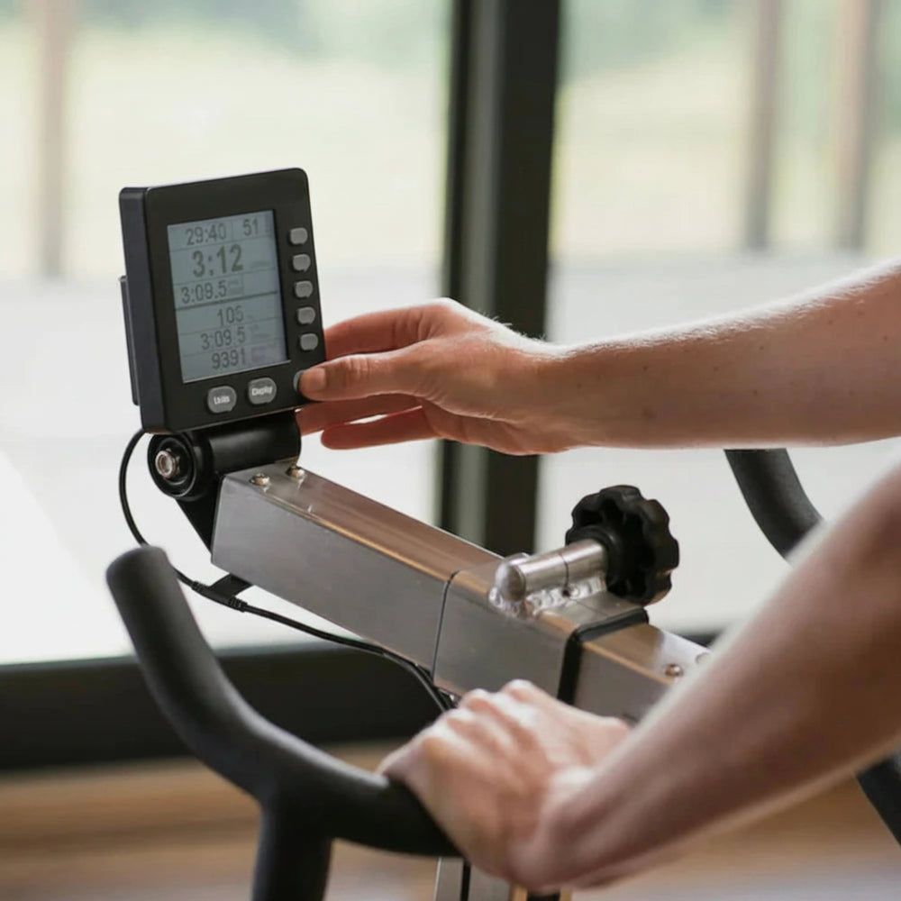 Person adjusting settings on a cycling machine with a digital display.