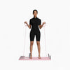 Woman using a pink pilates reformer board on a white background