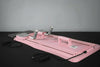 Pink pilates exercise board with gray handles on a black surface against a gray background