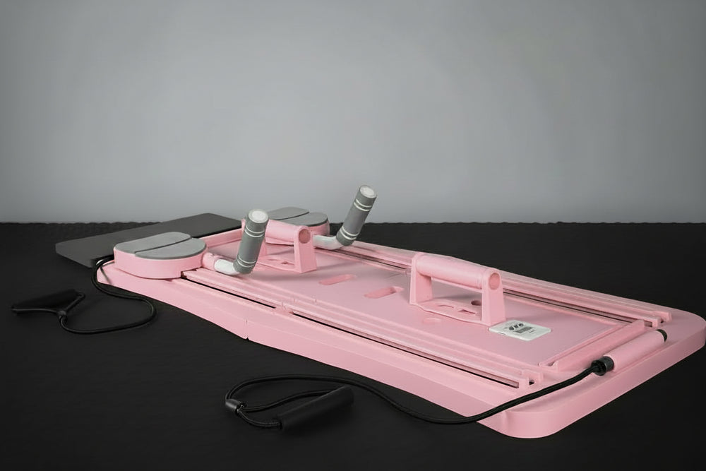 Pink pilates exercise board with gray handles on a black surface against a gray background