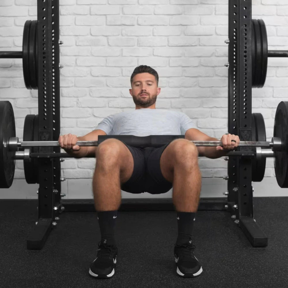 Man using squat pad on barbell rested on his lap in a gym setting