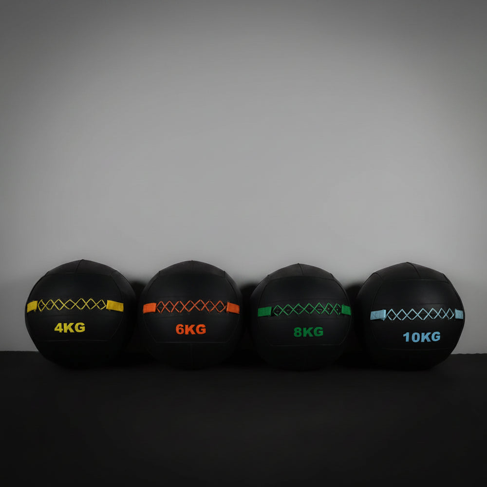 Four black slam balls with colour coded weights against a grey wall