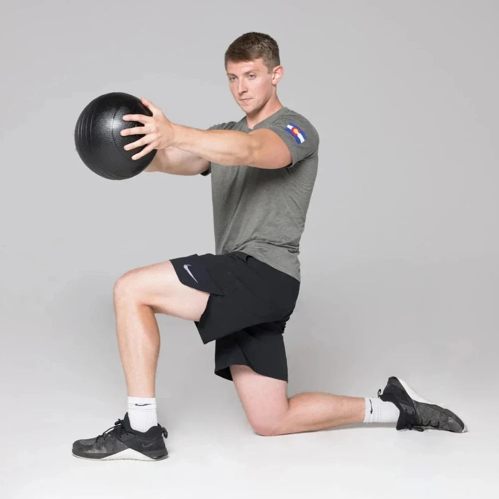 Man performing a workout with a slam ball on a grey background