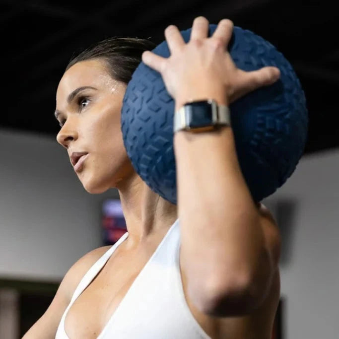 Woman holding a blue threaded slam ball in a gym setting
