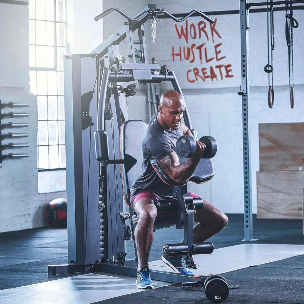 Man exercising with dumbbells on a machine in a gym with motivational quote on wall