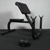 Black weight bench with weights and barbell on a dark floor.