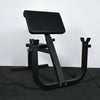 Angled view of preacher curl bench on a black tiled floor