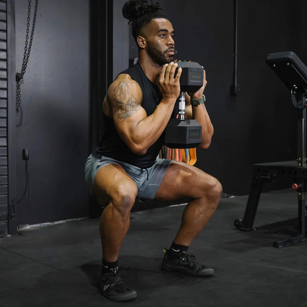 Man performing a squat with dumbbells in a gym setting