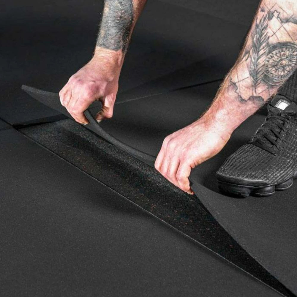 Man lifting thick black gym floor tiles