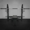 Weight bench with barbell on a dark floor and gray wall