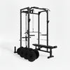 Black gym power rack with weight plates and bench on a white background