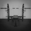 Weight bench with barbell on a dark floor and gray wall background