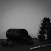 Gym equipment including weight plates, dumbbells, and a barbell on a dark surface with a gray background.