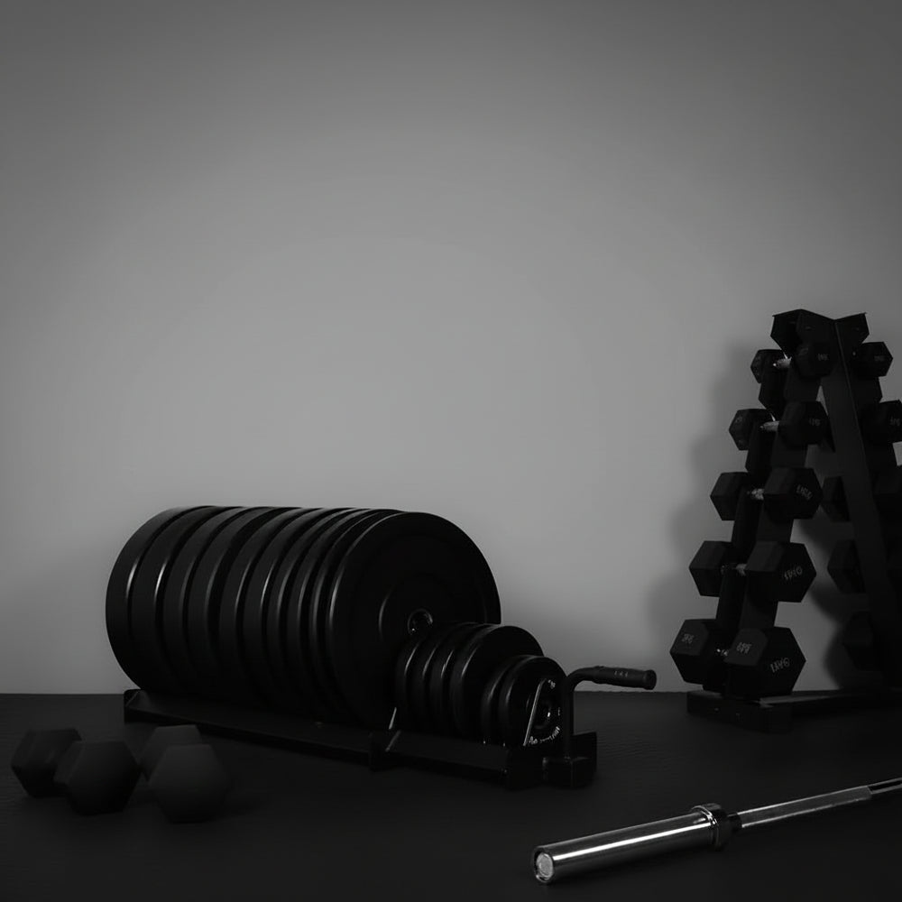 Gym equipment including weight plates, dumbbells, and a barbell on a dark surface with a gray background.